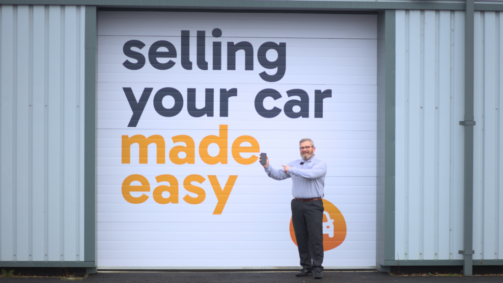 Man holding car keys up in front of a car buying crew sign